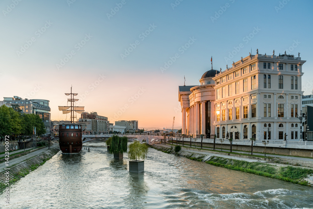 Wide view of the center of skopje Macedonia with the river Vardar, ship and surrounding buildings, late afternoon with sunset. - obrazy, fototapety, plakaty 