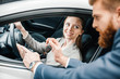© LIGHTFIELD STUDIOS - Bearded salesman giving car key to smiling young woman sitting in new car