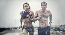 Muscular Male And Female Athlete Covered In Mud Running Down A Rough Terrain With A Desert Background In An Extreme Sport Race 