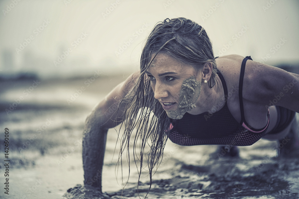 Strong athletic woman laughing with mud on her face crawling in mud or extreme sport with with grungy texture  - obrazy, fototapety, plakaty 