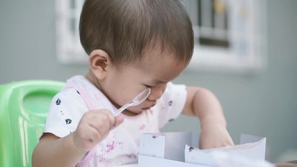 Wall Mural - 1 year old Asian baby eating cake with plastic spoon by himself