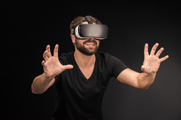 Wall Mural - Young bearded man in black t-shirt wearing virtual reality headset on black