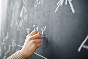 Closeup shot of male hand writing algebraic formula on blackboard with chalk
