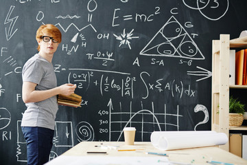 portrait of young red haired student working at big blackboard writing science formulas in college c
