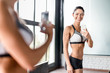 © pressmaster - Portrait of proud muscular  woman smiling boasting her fit figure and slim waist taking selfie in gym mirror and posing