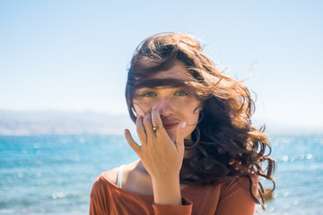 Portrait of happy smiling young woman on beach and sea background. Wind plays with girl long hair