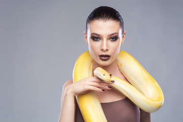 Beautiful brunette woman with a albine python. Fashion makeup, gray background