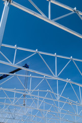 Crane lifting galvanized steel roof truss construction frames with deep blue sky in the background