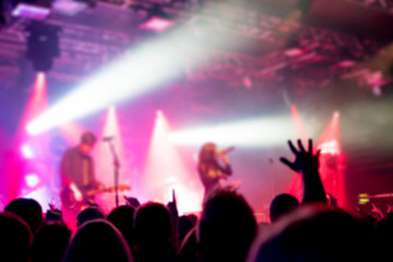 Blurred background, Bokeh, silhouette of cheering audience, hands up and musicians on the stage with lighting in indoor concert