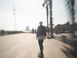 © Daniel - Young blonde modern woman with leather jacket riding her skateboard at the boardwalk of Barcelona motion blur