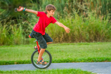 Outdoor Portrait Of Young Boy Riding A Unicycle On Natural Background