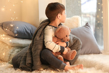 Cute Little Boy With Teddy Bear Near Window At Home