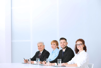 Sticker - Group of four business people in elegant suits sitting at working desk in light auditorium