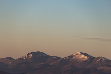 a minimalist view of some mountains top with snow, under a big, almost empty sky, with golden hour w