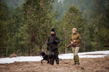 two hunters armed with a rifles, walking in a snowy winter forest.