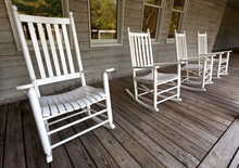Four White Rocking Chairs On Wooden Porch.