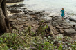 © lookproduction - Young woman in blue dress staying on the rocky beach