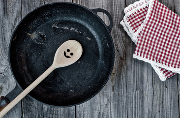 Wall Mural - Black cast-iron frying pan with a wooden spoon on a gray wooden surface