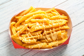 Paper red box full of delicious french fries with cheese sauce on white wooden background