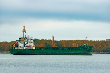 Green cargo ship moving to the port in cloudy day