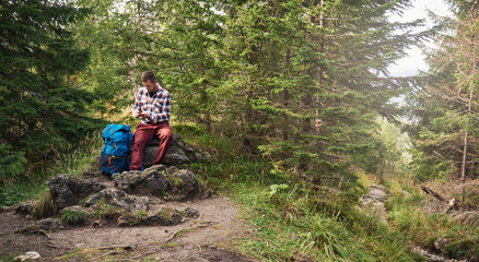 Wall Mural - Hiker sitting on a rock using cellphone gps