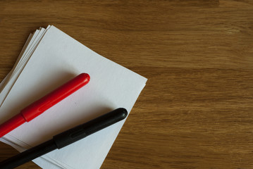 Red and black markers and white sticky note on wooden table. Copy space