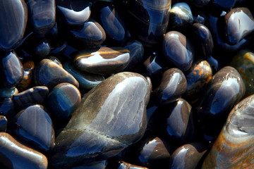 Sun reflections on round and oval shaped black and brown stones on the beach