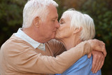 Fototapeta  - Affectionate seniors in love hugging and kissing outdoors