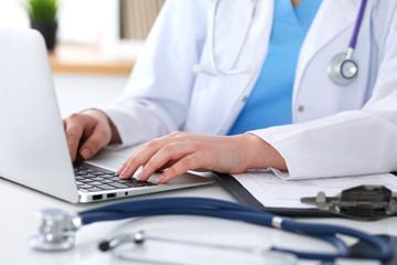 Wall Mural - Close up of unknown female doctor typing on laptop computer while sitting  at the table. Medical staff, compulsory work concept