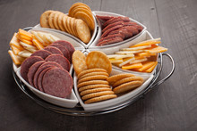 White Platter Of Crackers, Cheddar Cheese, And Sliced Meat On Dark Wooden Background Horizontal Shot 