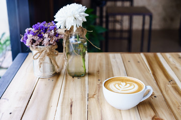 Wall Mural - Latte art coffee in white mug on wood table in coffee shop.