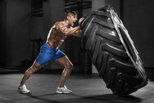 Muscular man working out in gym flipping tire, strong male naked torso abs