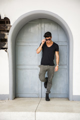 Wall Mural - Handsome young man outdoors in front of old house's wood entrance door, looking away to a side