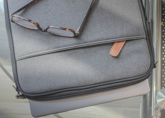 grey laptop case sits on brown table next to old book and notepad and journal ready for digital nomad to begin entrepreneur business. laptop case is soft and has zipper with pocket on laptop case.