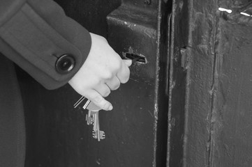 Hand use the key for unlocking door. Monochrome photo.