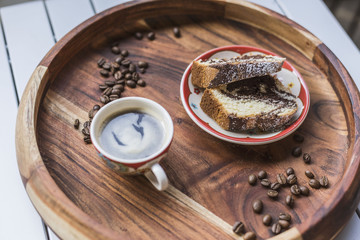 A cup of fresh espresso and a cake with coffee beans on the sides on a wood table background 