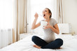 Happy pregnant young woman eating ice cream on bed
