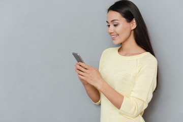 Wall Mural - Happy attractive young woman standing and using mobile phone