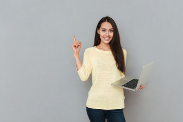 Sticker - Smiling beautiful young woman holding laptop and pointing away