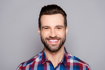 A close up portrait of young happy cheerful young man in checkered shirt in front of gray background