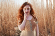 beautiful young woman with long cascading red hair and sultry looks posing in a field of Elephant Grass
