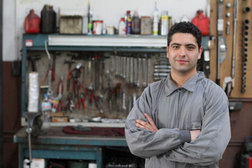 Man wearing overalls in a garage with tools in the background