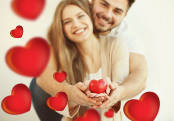 Poster - Young couple holding small red heart, on light background