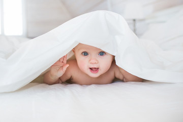 Pretty Infant hides under a white cover in bed in bedroom