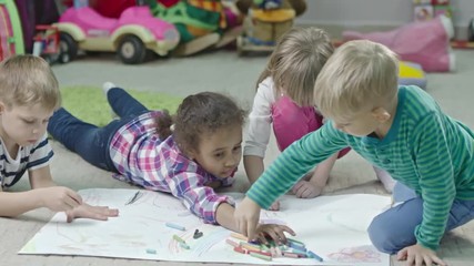 tracking shot in slow mo of little children sitting and lying on the floor in play room and drawing 