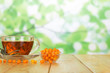 © laboko - A bowl of berries of sea-buckthorn berries, Cup of tea and leaves on abstract green background.