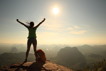 silhouette of cheering woman hiker open arms at mountain peak