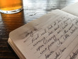 Handwritten journal open on wooden table next to glass of beer