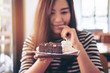 A beautiful asian woman holding brownie cake and whipped cream with feeling happy and good lifestyle in the modern cafe