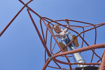 Wall Mural - Active young child girl climbing the spider web playground activity. Children summer activities.